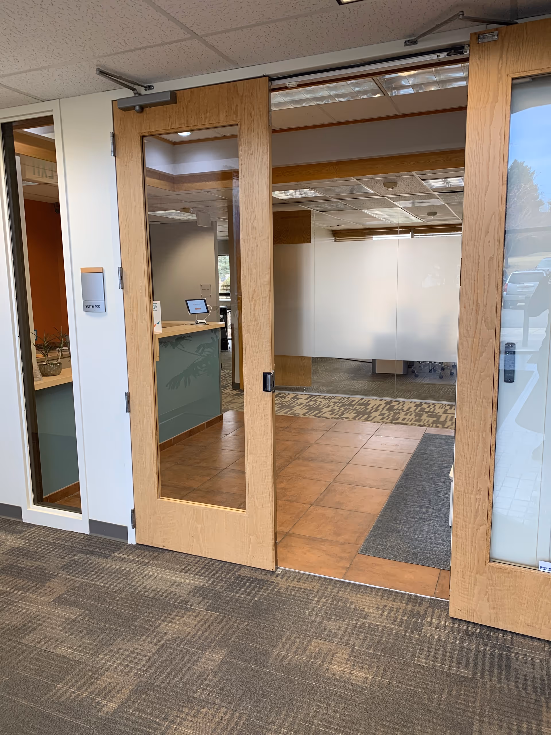 Double wood doors with glass panels open to a tiled lobby with reception desk.