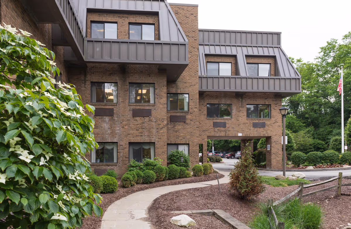 Brick senior living facility exterior with angular balconies and a landscaped walkway to a covered entrance.