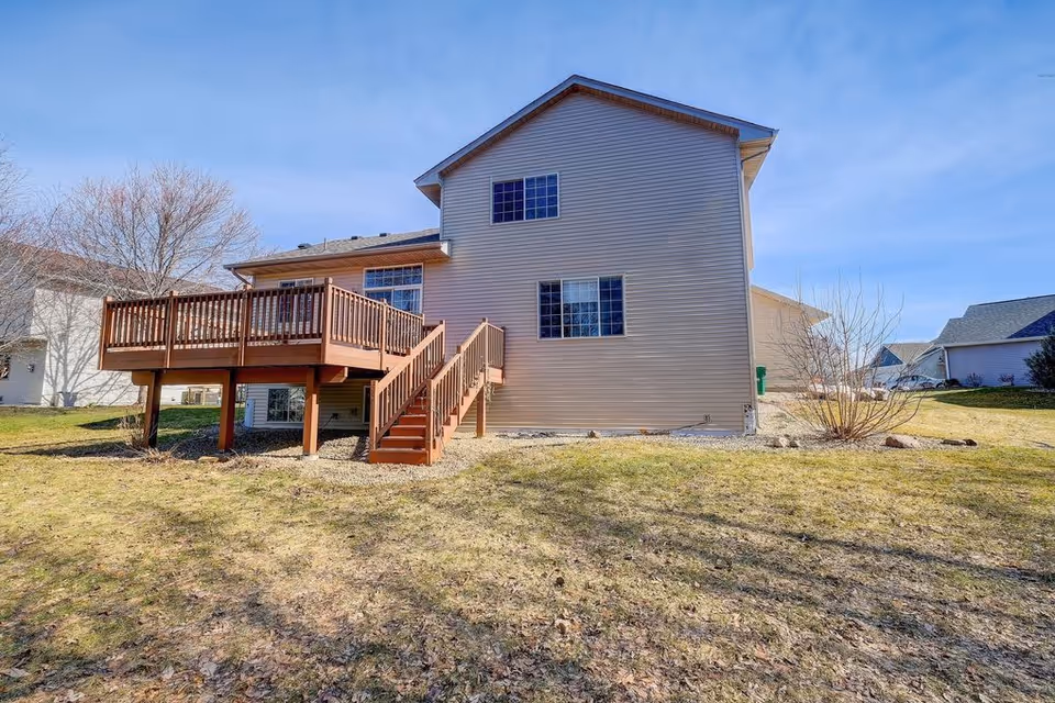 Back view of a two-story beige house with a wooden deck and stairs.