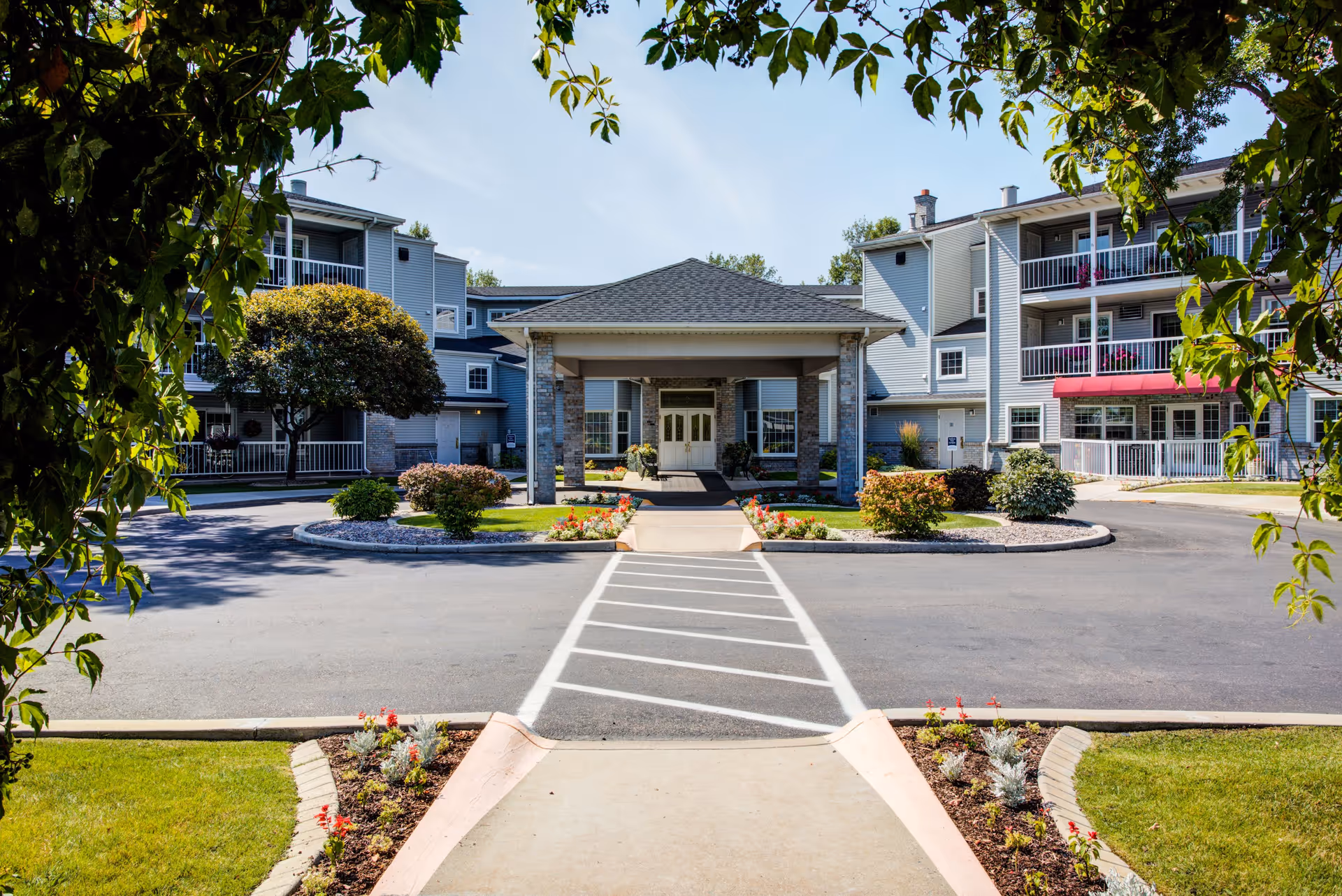 Covered main entrance and circular driveway of a multi-story senior residence with balconies and landscaped grounds.