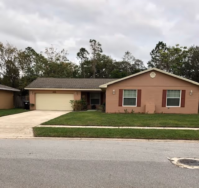 Single-story brick suburban house with a two-car garage, front lawn, and overcast sky.