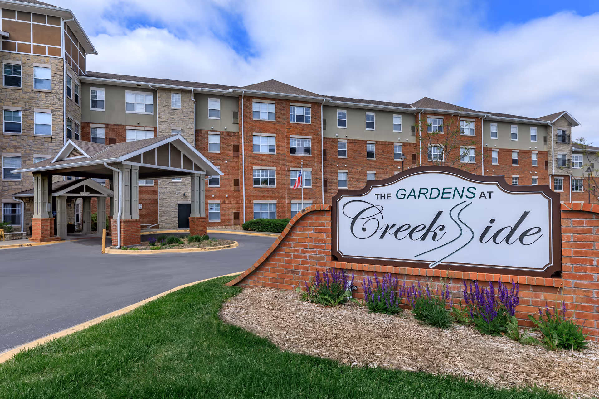 Exterior view of The Gardens at Creekside with brick building and large sign.