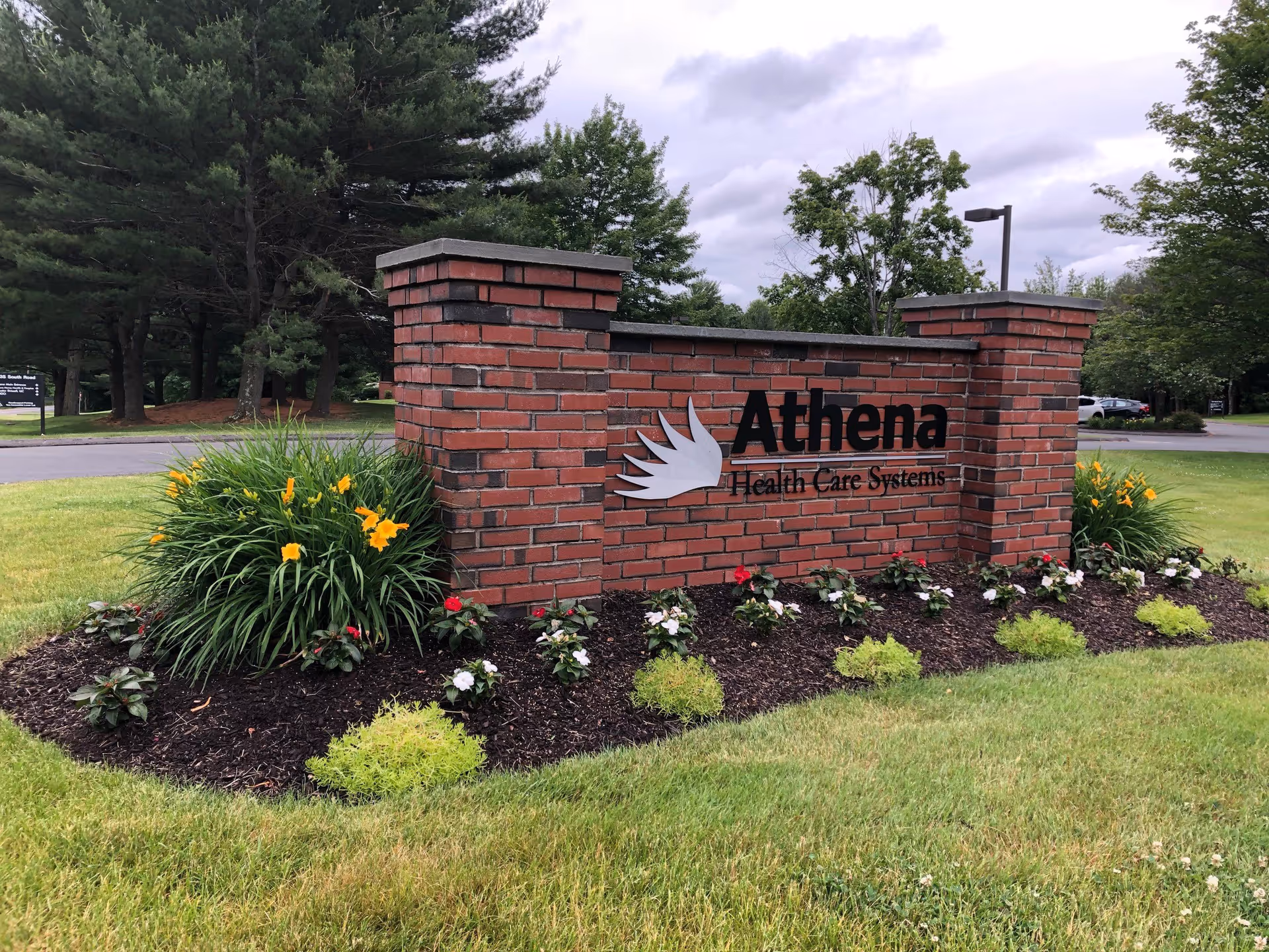 A brick Athena Health Care Systems sign stands amid manicured flowers and trees.