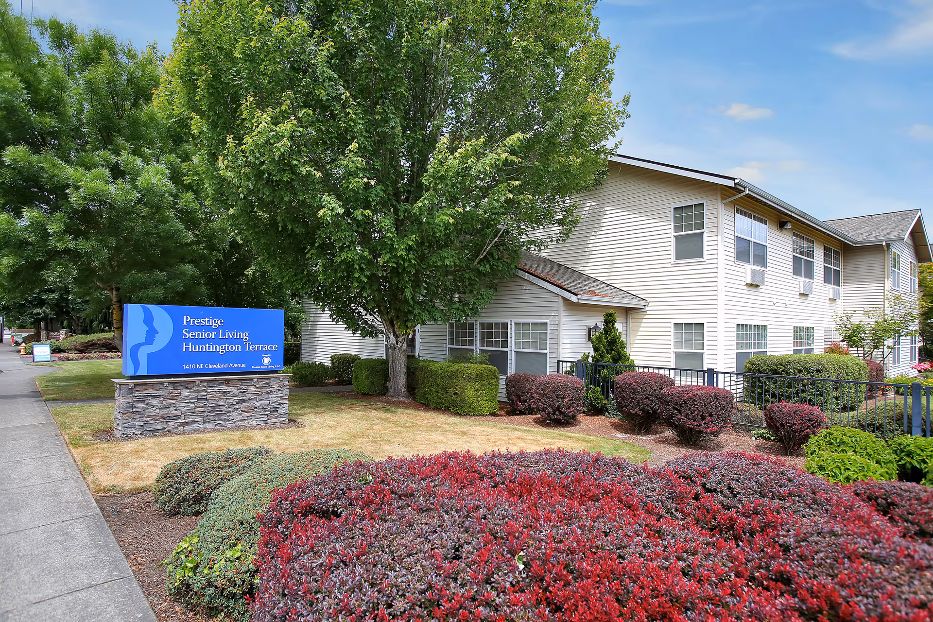 Exterior view of Prestige Senior Living Huntington Terrace with a blue sign and landscaped grounds.