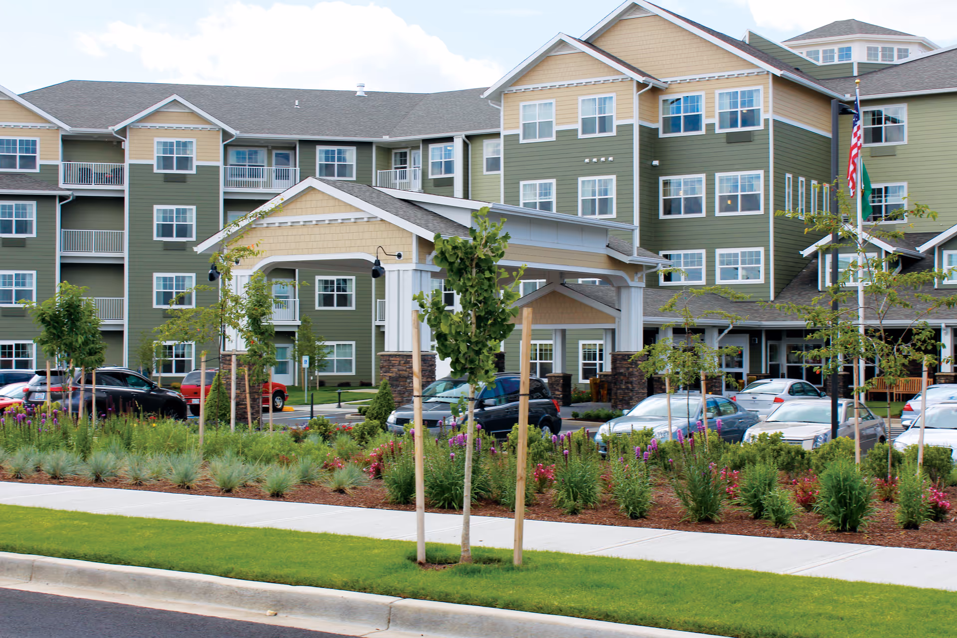 Exterior view of a multi-story senior living facility with landscaped entrance and parking.