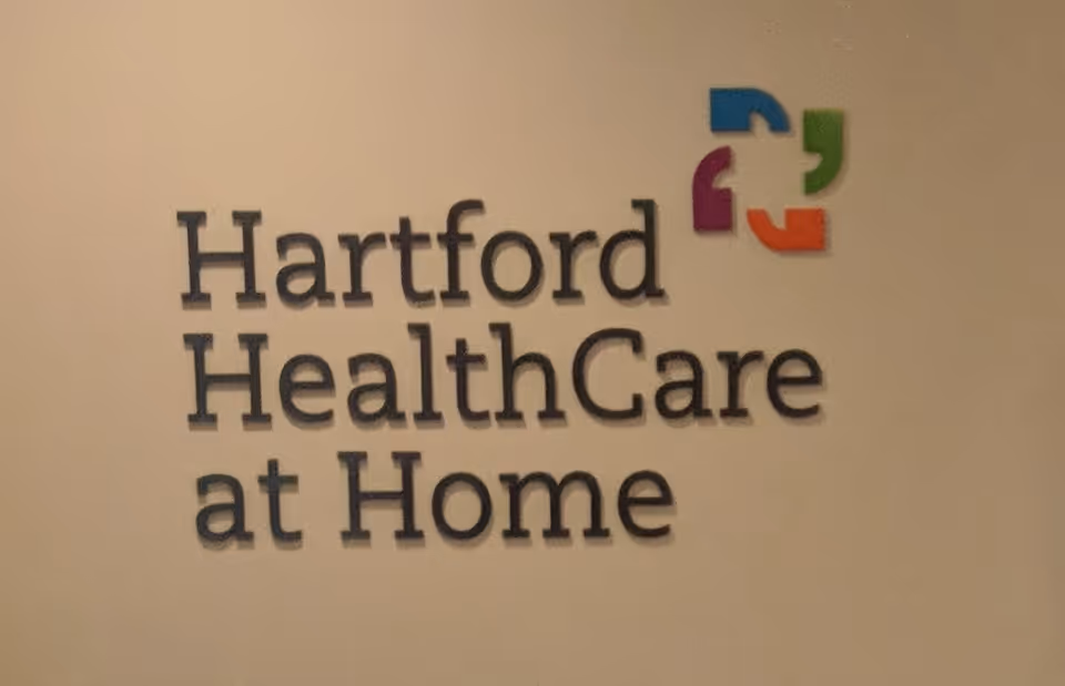 Wall sign reading Hartford HealthCare at Home on a beige interior wall.