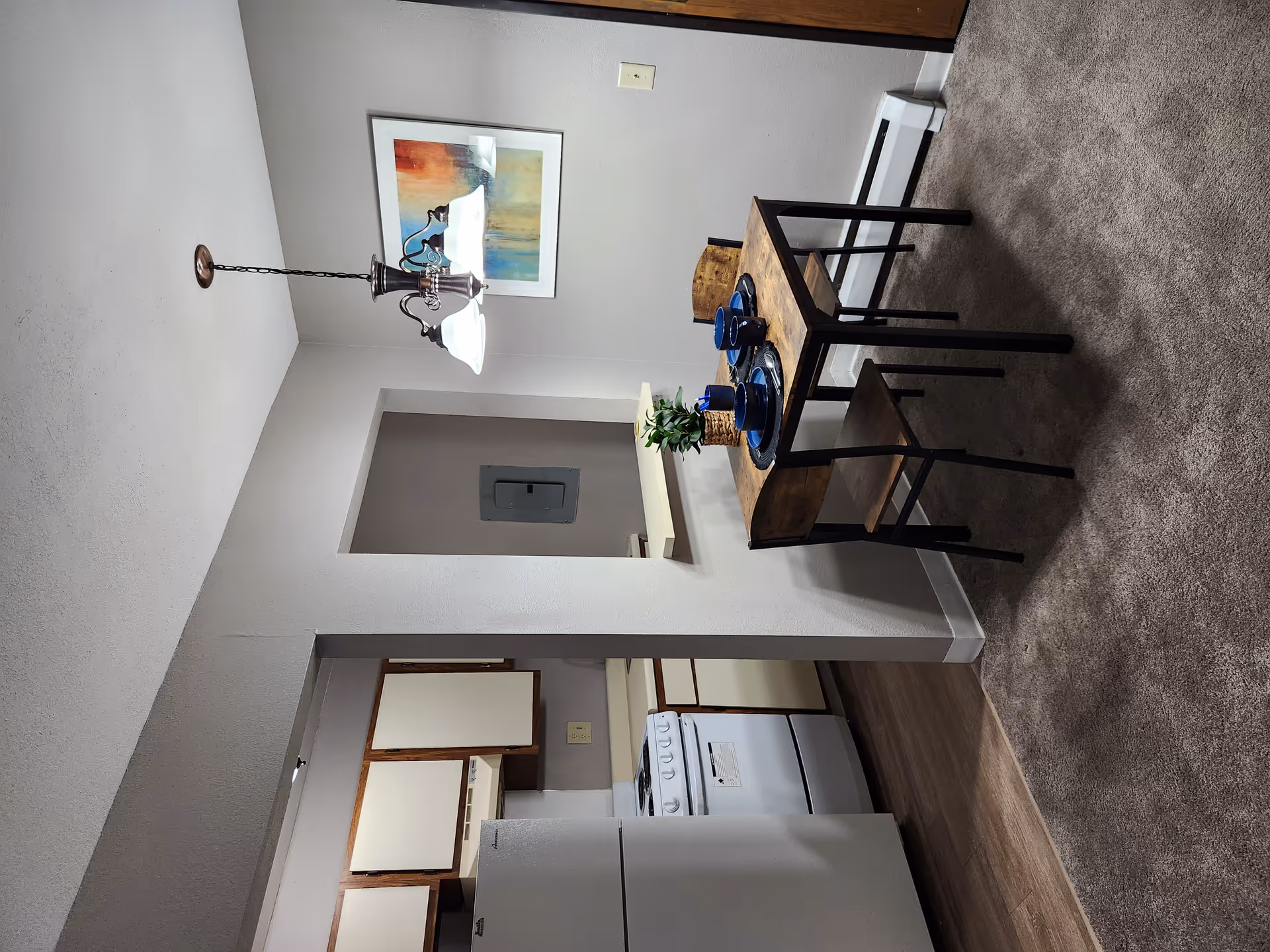 An interior dining area with a wooden table, blue dishes, plant, and visible kitchen.