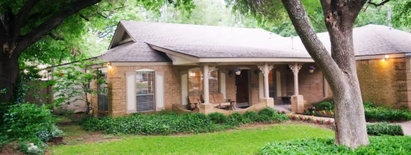 Single story brick senior living facility with a front porch and surrounding greenery.