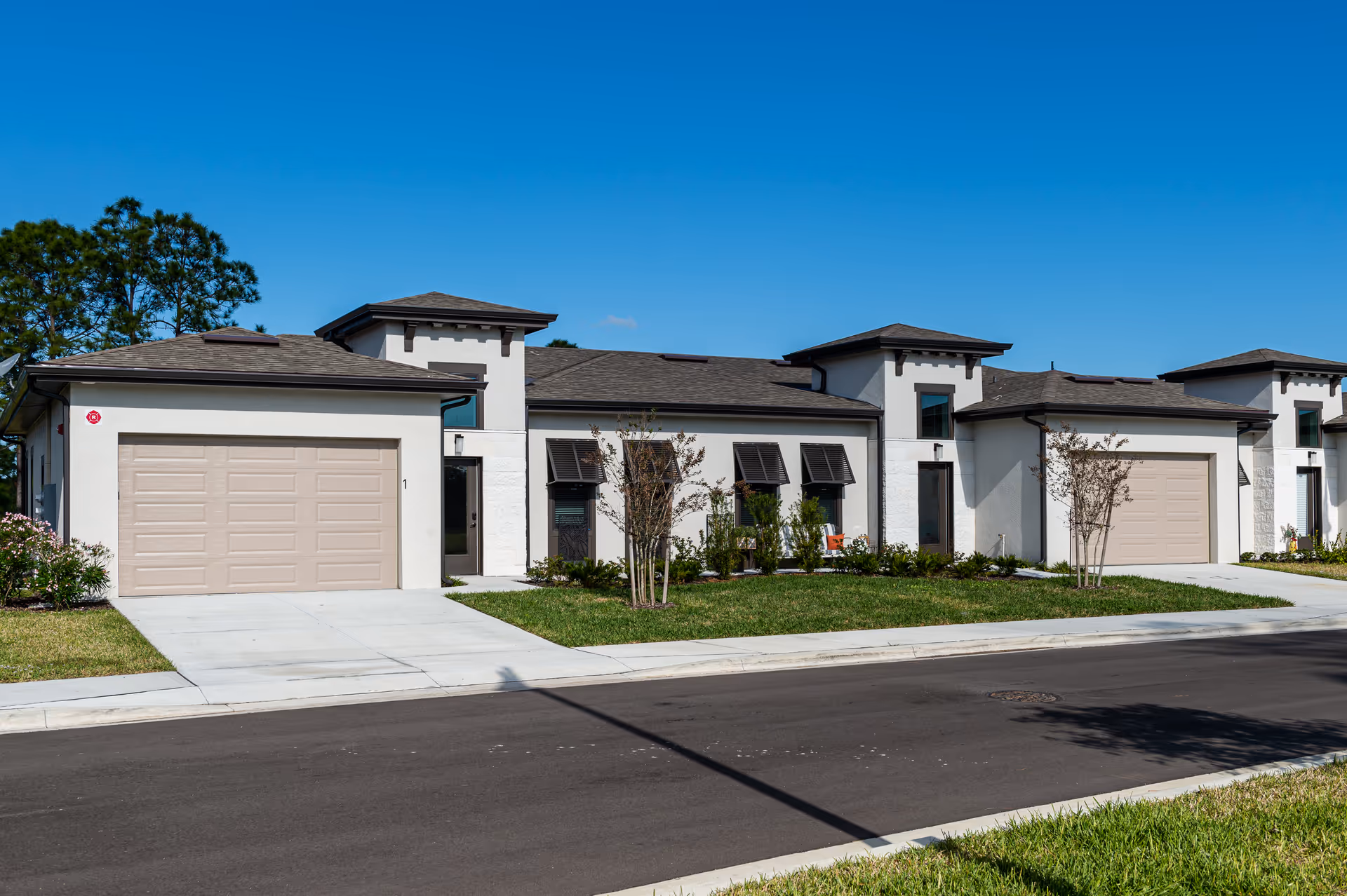 Row of modern, white townhome-style buildings with beige garages along a sunny street.