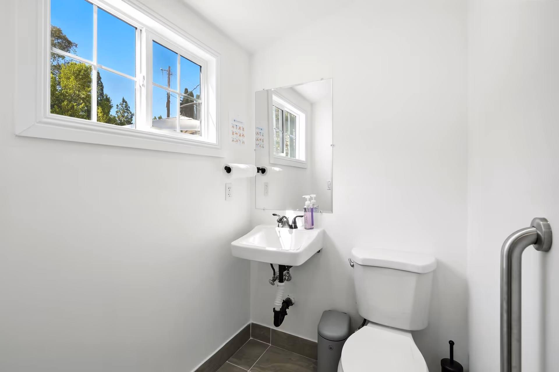 Bright, minimal bathroom with sink, mirror, toilet, and window in an assisted living facility.