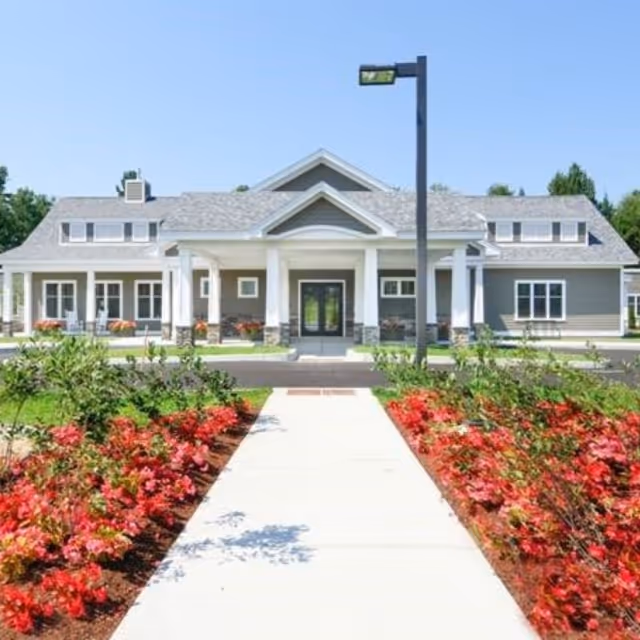 Front view of a modern senior living facility with a central entrance and landscaped walkway.