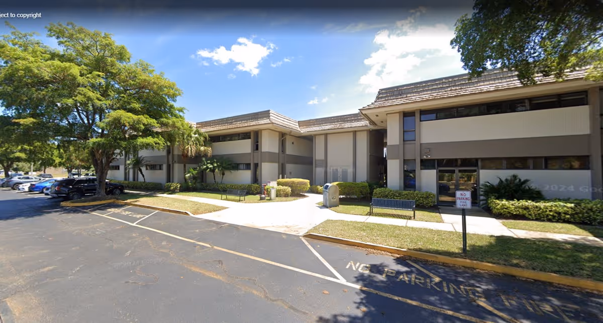 Exterior view of Senior Helpers South Palm Beach building with parking, trees, and walkway.