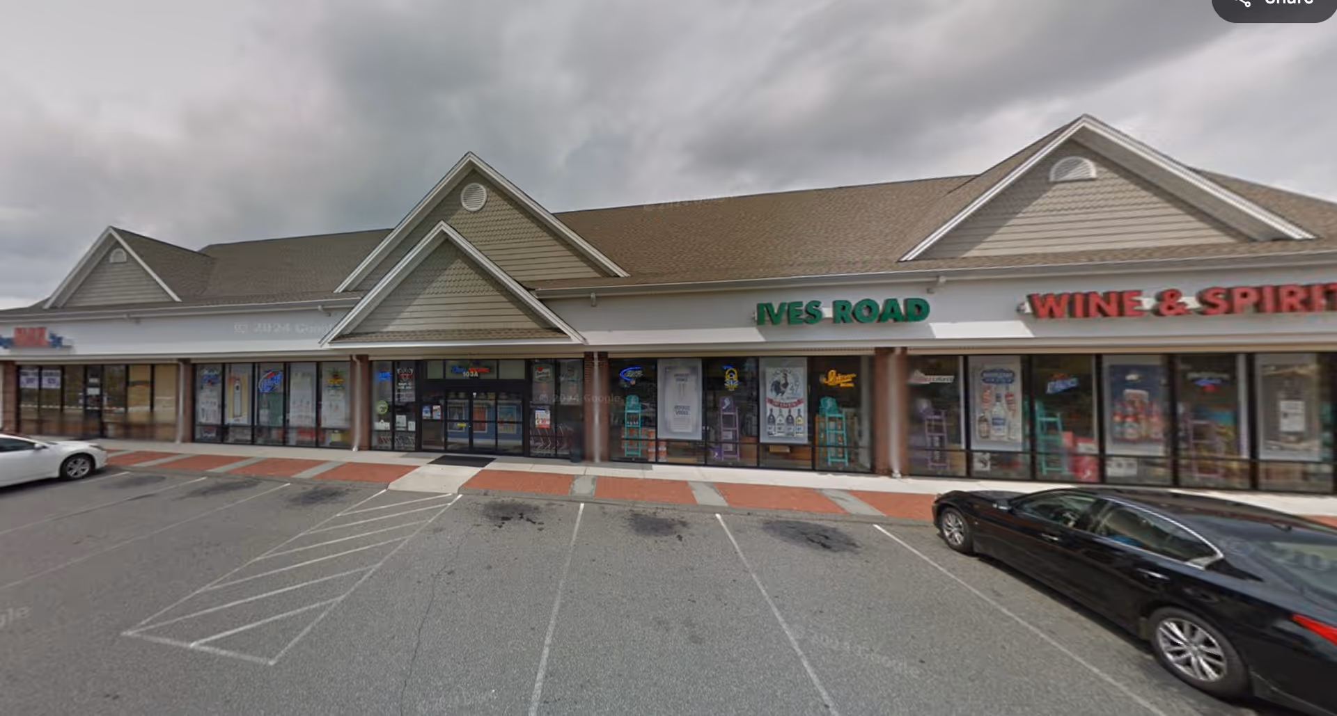 Exterior view of a strip mall storefront row with parked cars and signs.