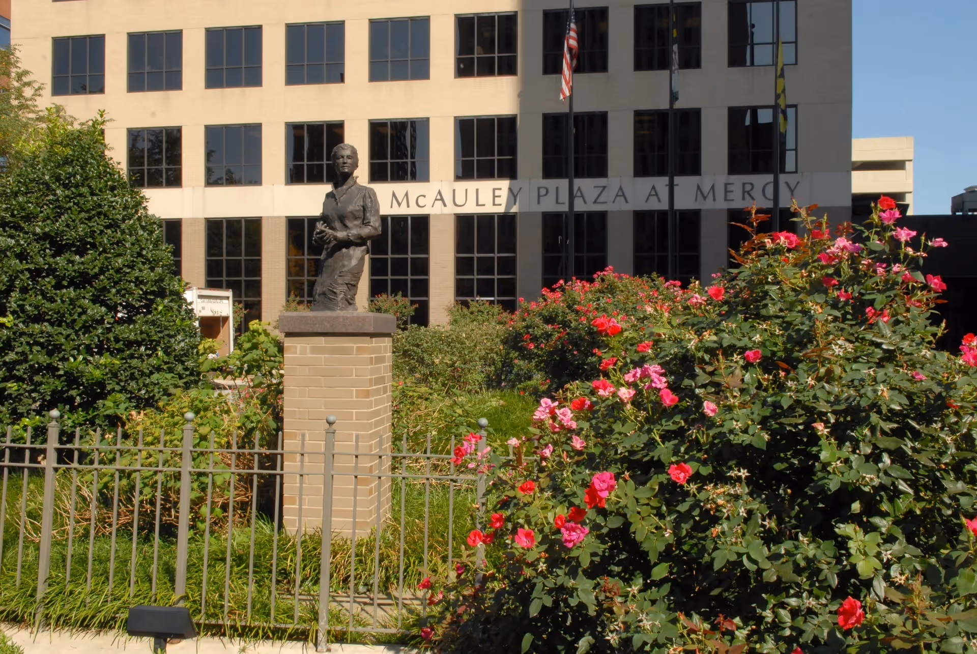 Front exterior of Mercy facility with statue, garden, and blooming roses.