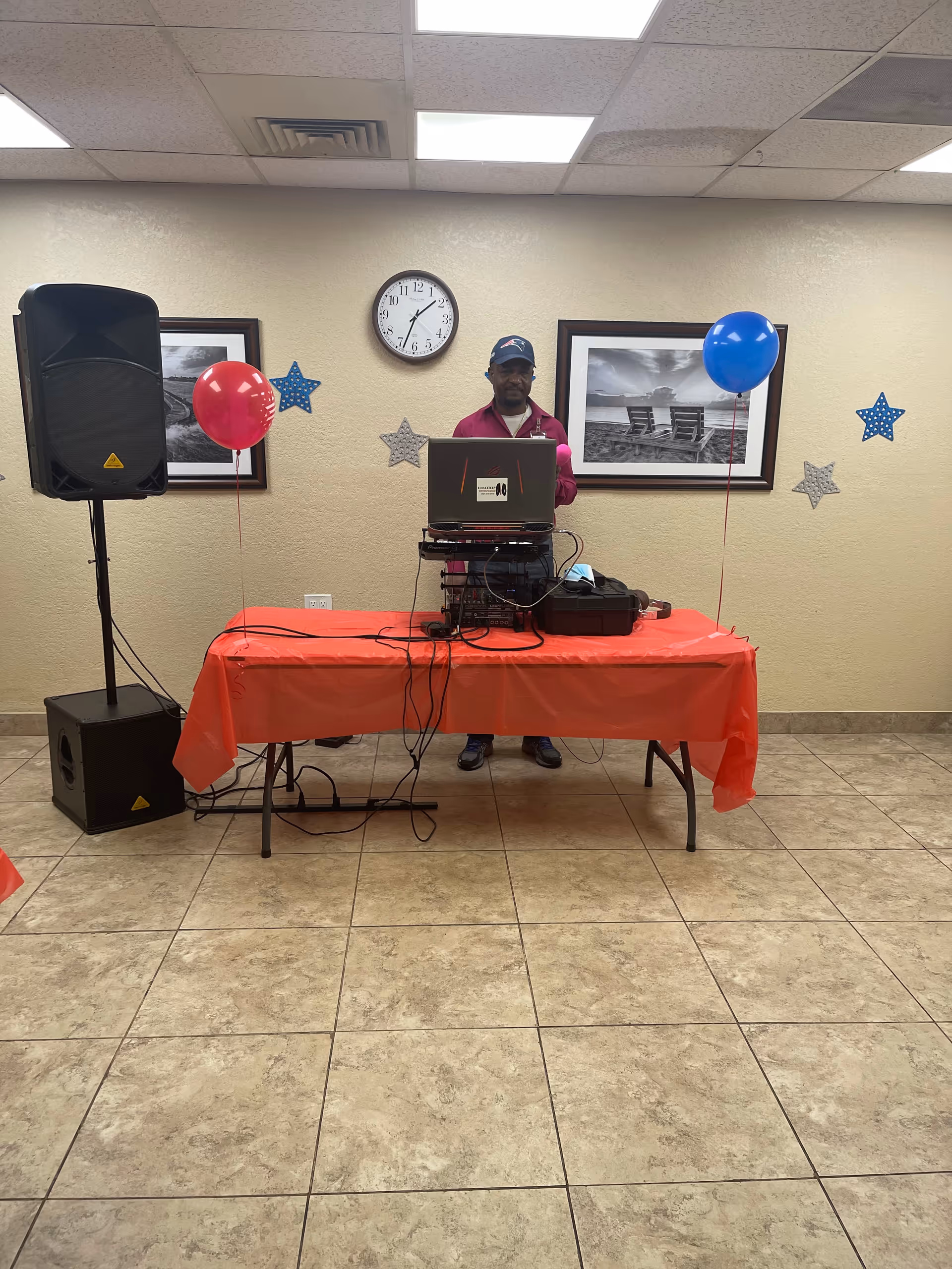DJ setup on a red tablecloth at Martin Coast Center event hall with balloons and photos.