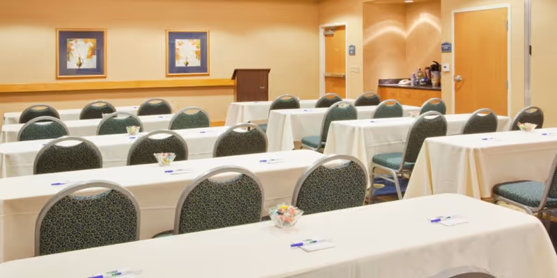 Empty banquet-style dining room with white-clothed tables and green chairs.