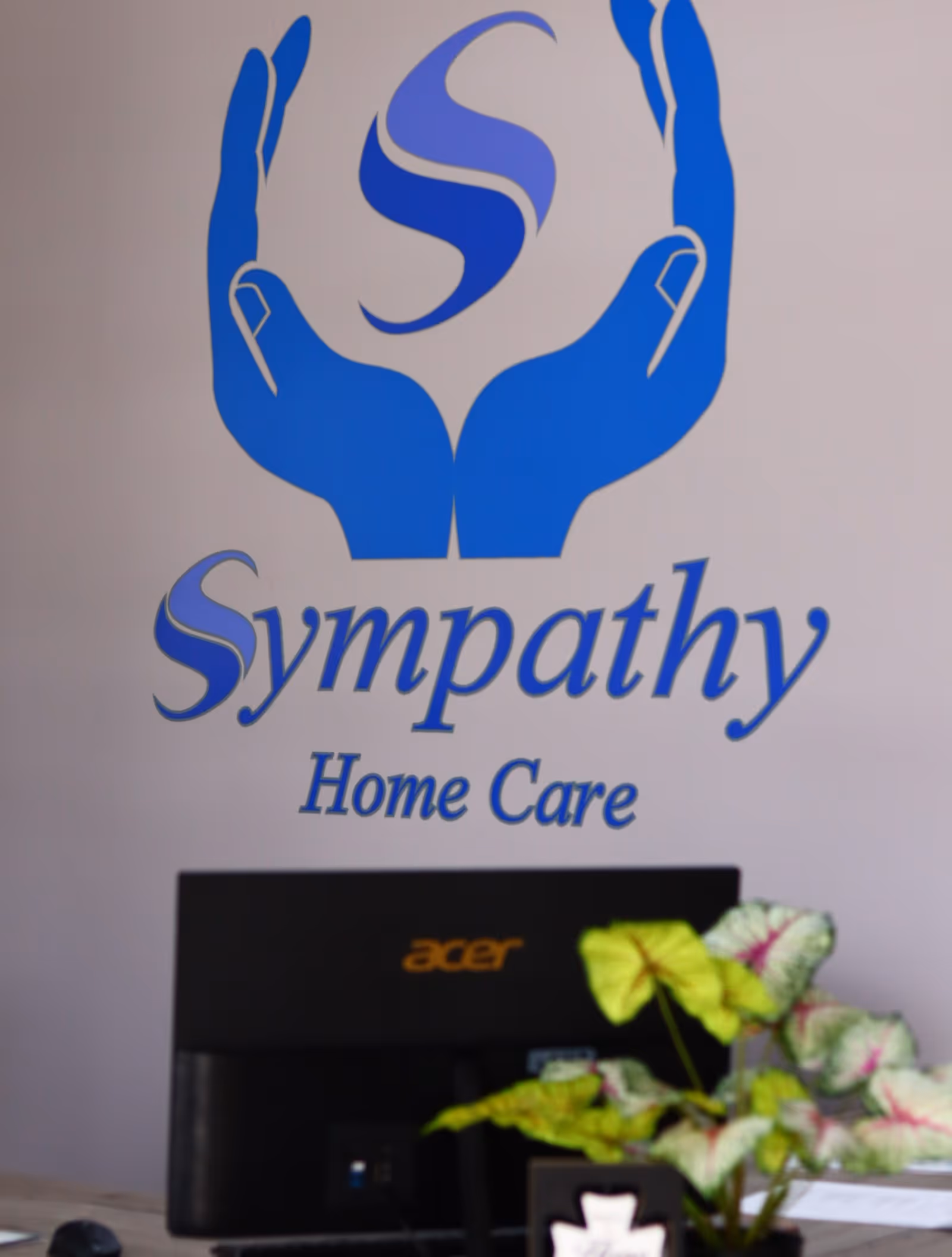 Blue hands logo and Sympathy Home Care text on wall behind a computer.