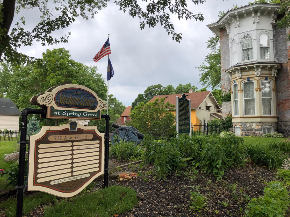Historic brick building with ornate bay window, a signboard, and lush greenery.