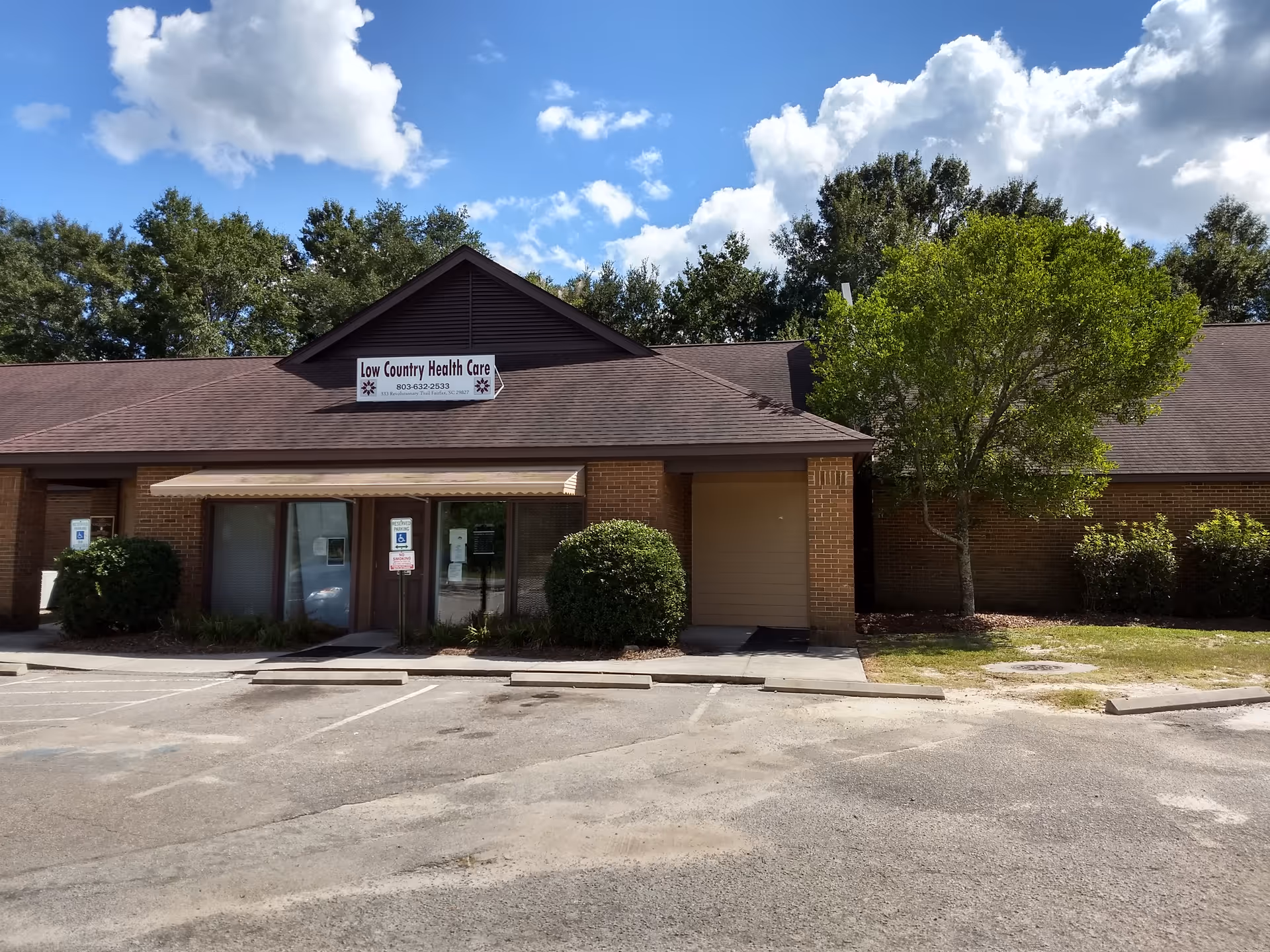 Exterior view of Low Country Health Care building with sign, parking, and trees.