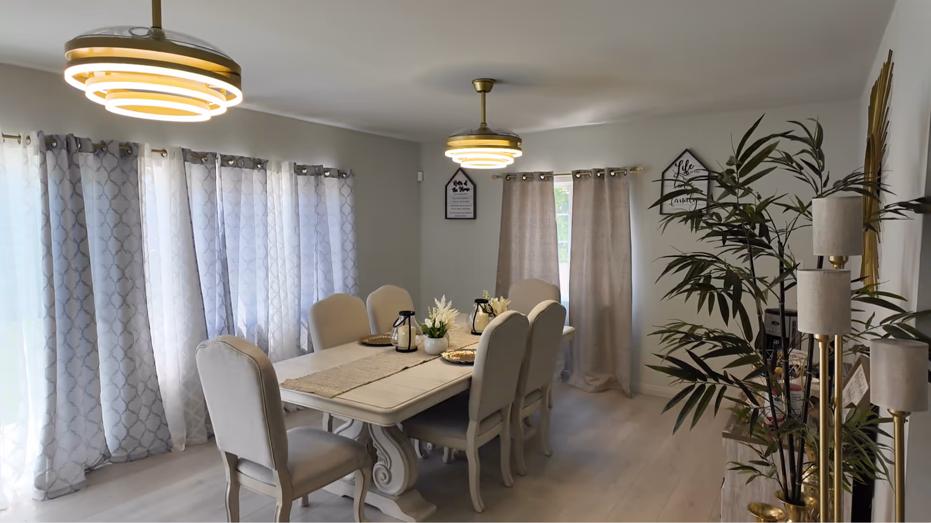 Well-lit dining room with upholstered chairs around a long table and potted plants.