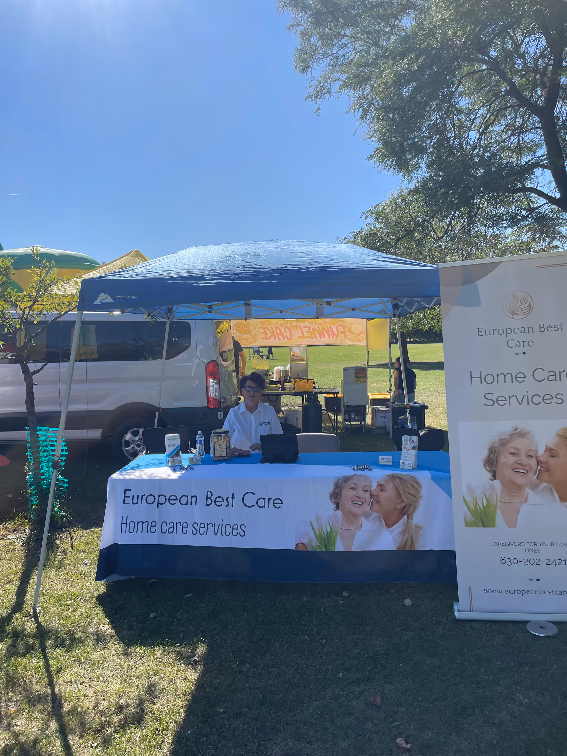 Outdoor booth with blue canopy, table, banner, and staff at European Best Care Home Care Services.