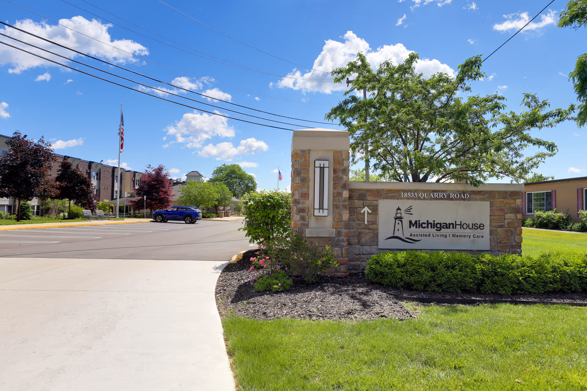 Exterior view of Michigan House Senior Living entrance with stone sign and landscaped grounds.