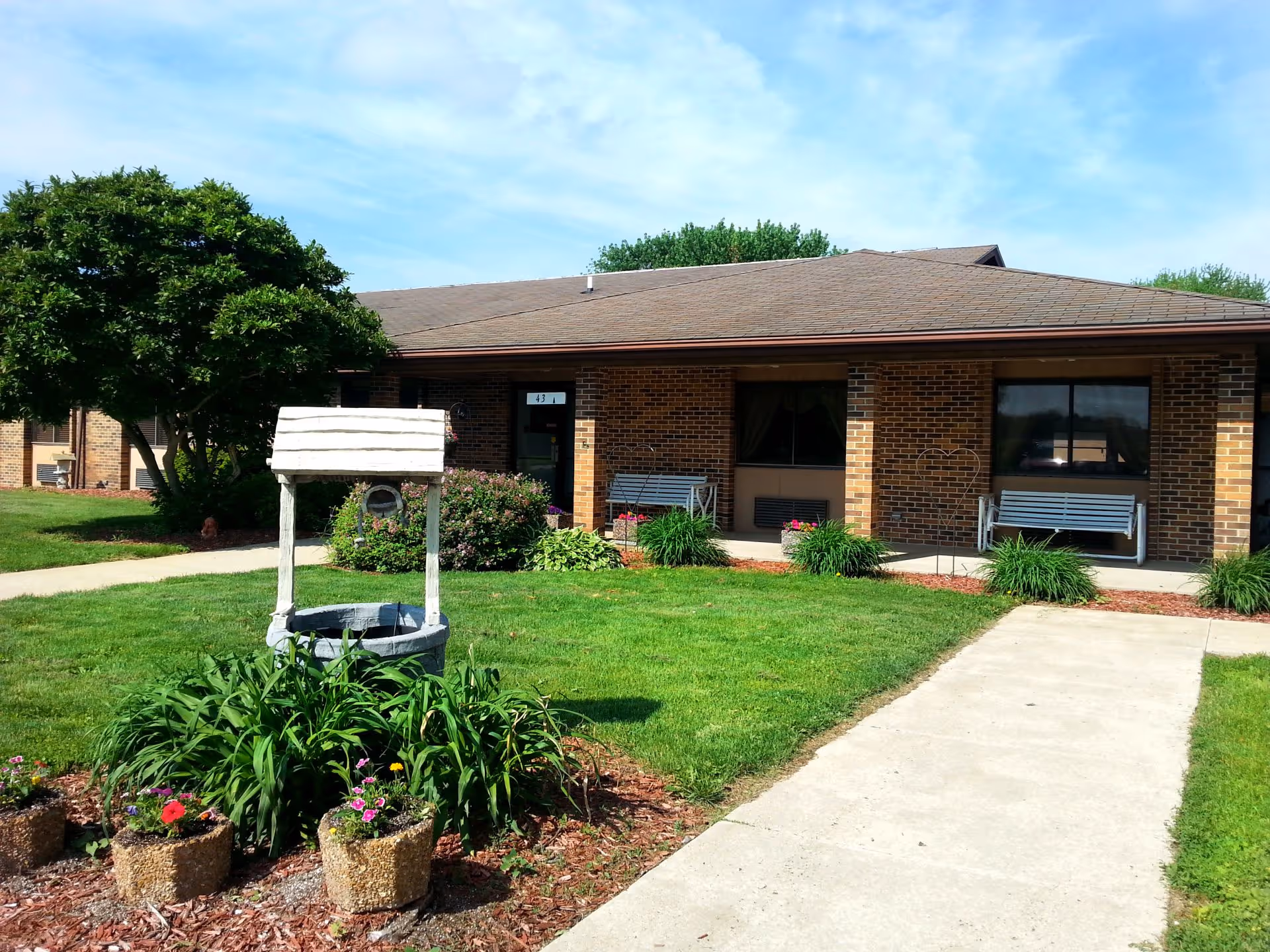 Single-story brick building front with a lawn, walkway, decorative wishing well and benches.