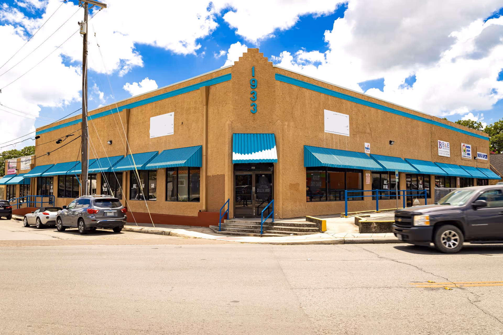 Exterior view of a tan building with teal awnings along a street.