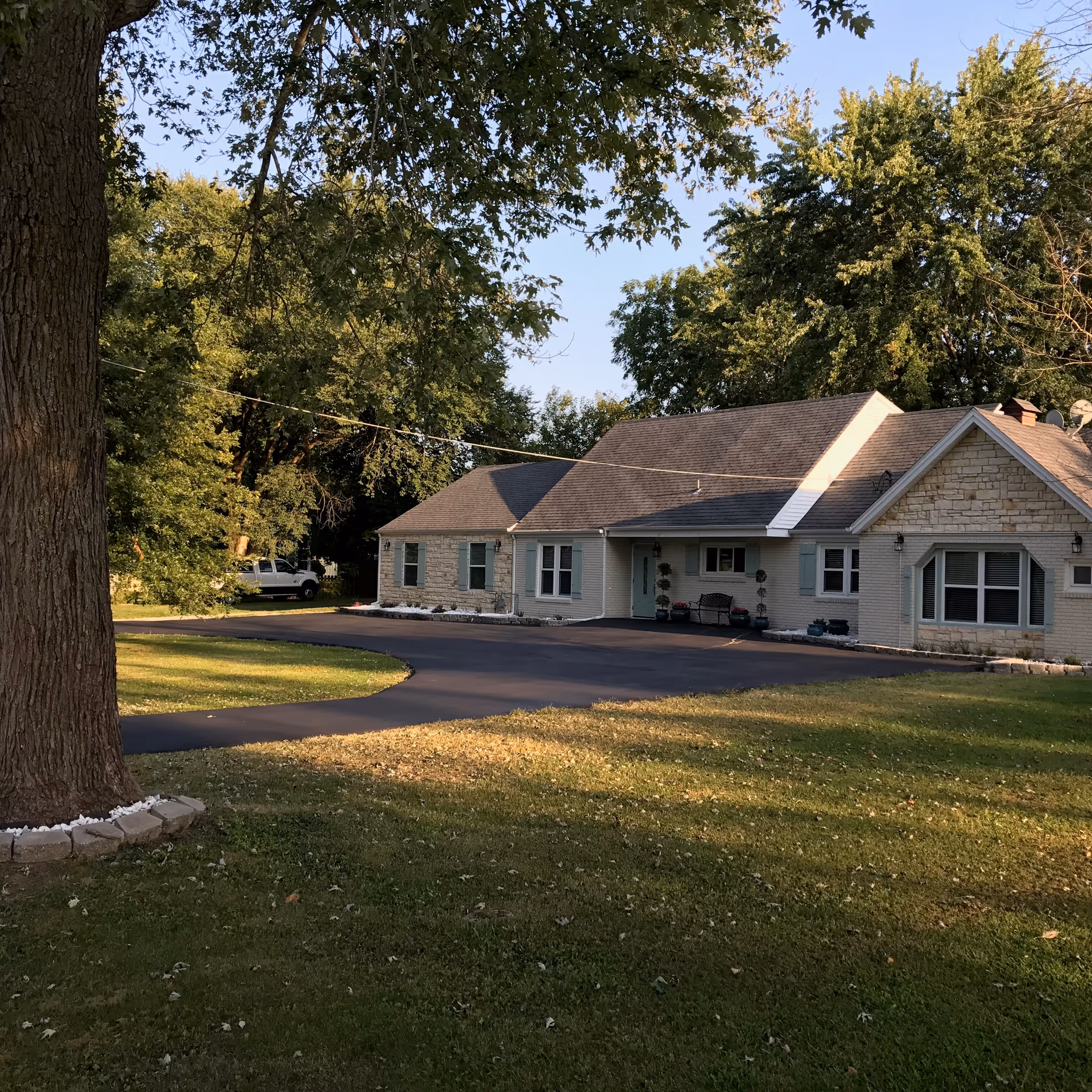 Single-story assisted living facility exterior with driveway, lawn, and large trees around the building.