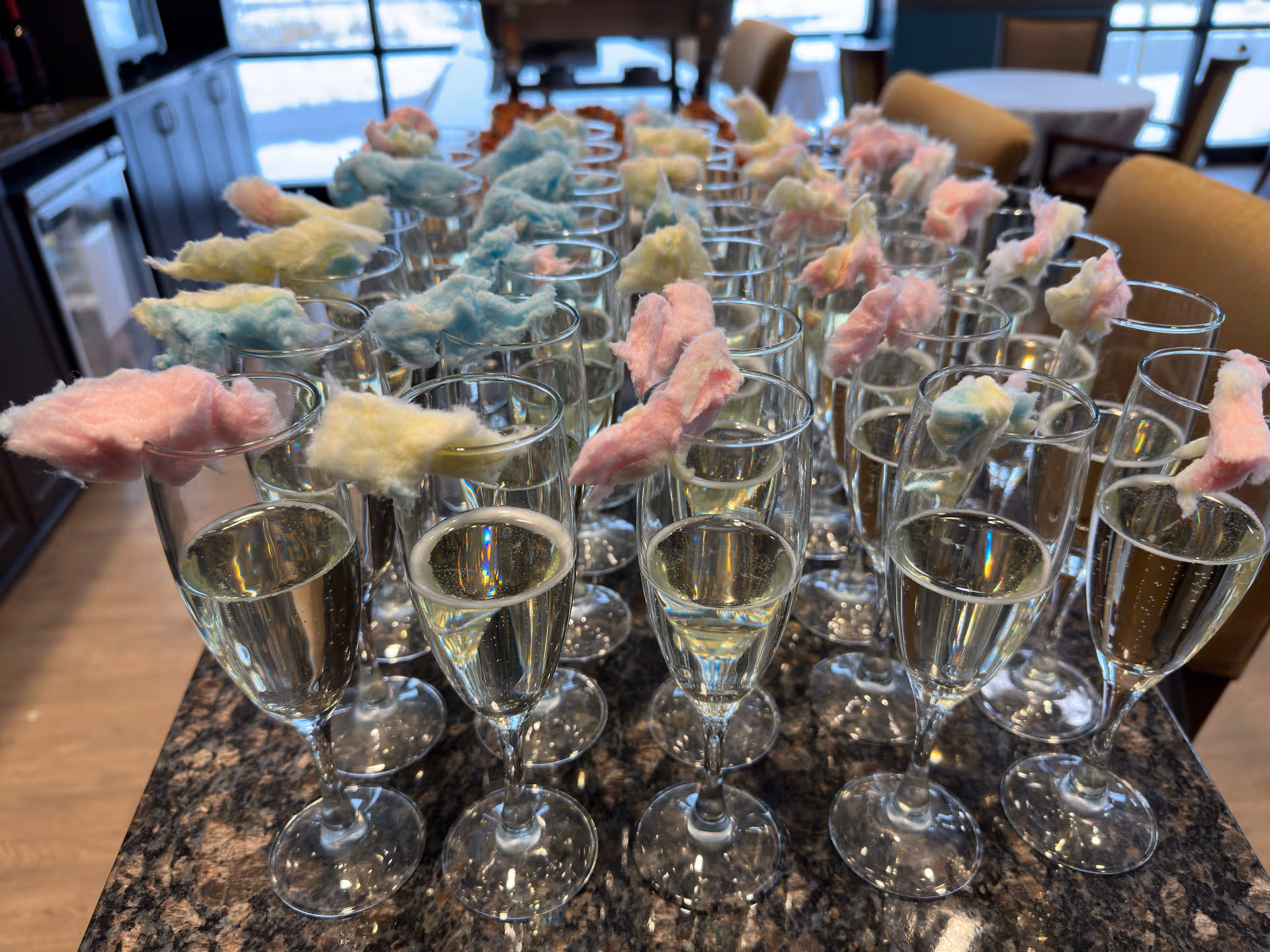 Rows of champagne glasses with pastel cotton candy toppers on a granite counter.