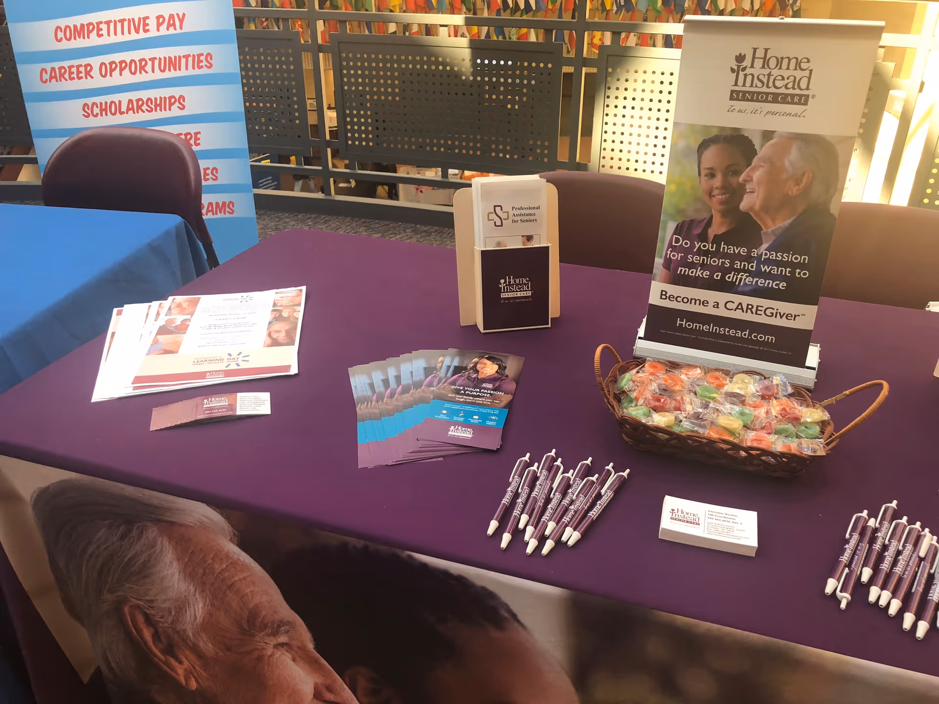 Indoor promotional table displaying literature, pens, and a Home Instead banner.