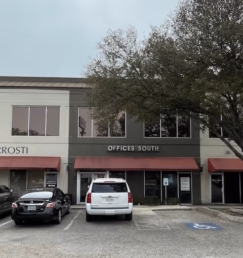 Exterior view of a two-story office building with red awnings and parked cars.