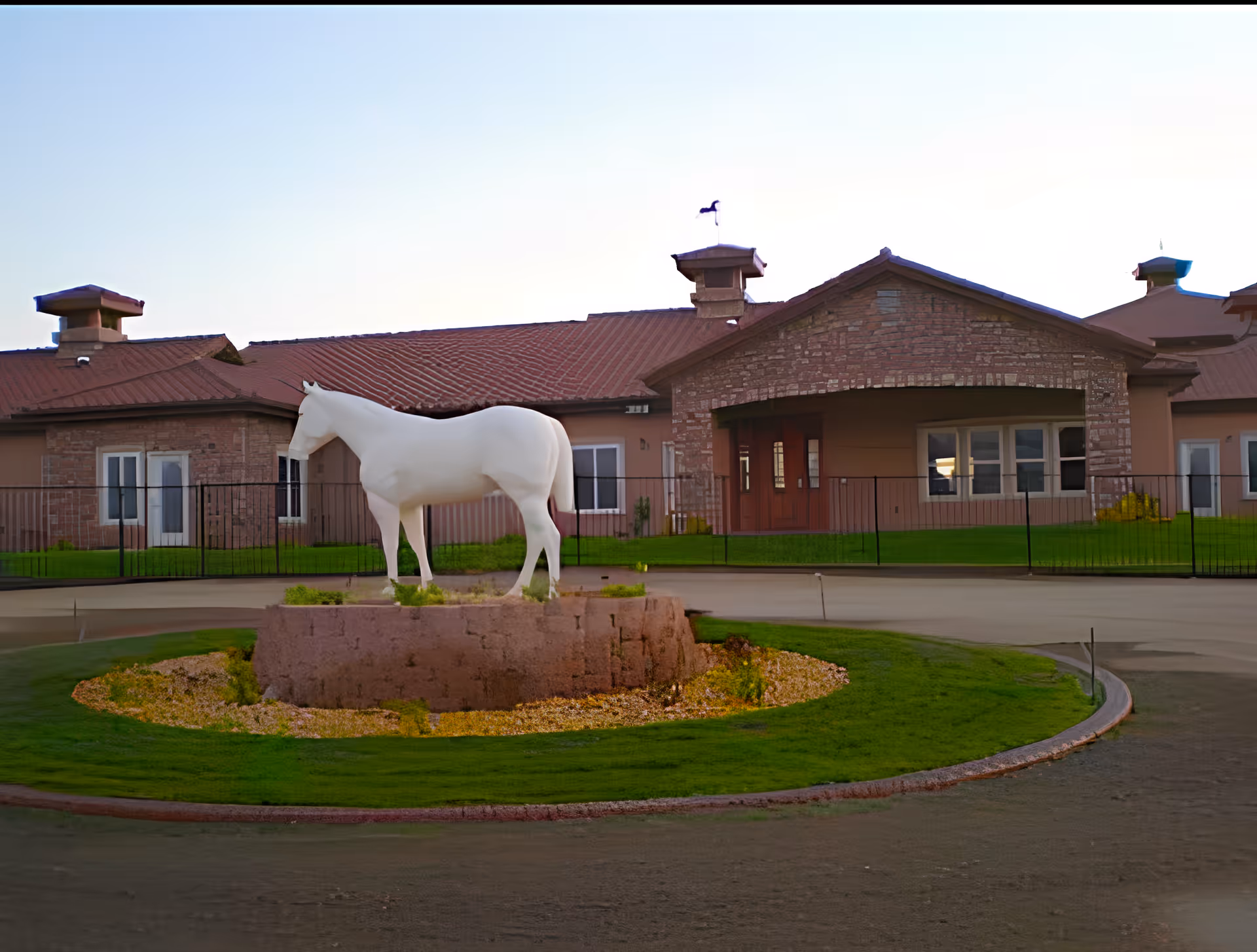 A white horse statue on a circular planter in front of a single-story brick senior living facility building.