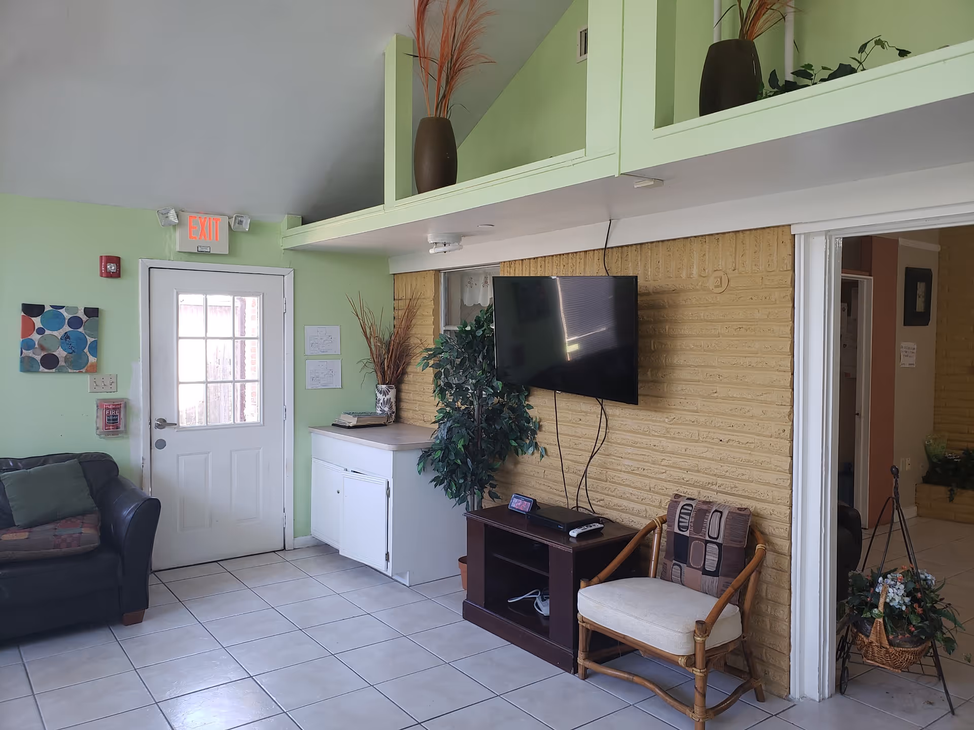 Bright living room area with couch, wall-mounted TV, plants, and entry door.