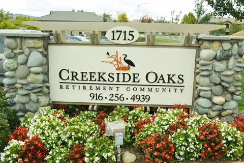 Creekside Oaks Retirement Community entrance sign with stone pillars and colorful flowers.