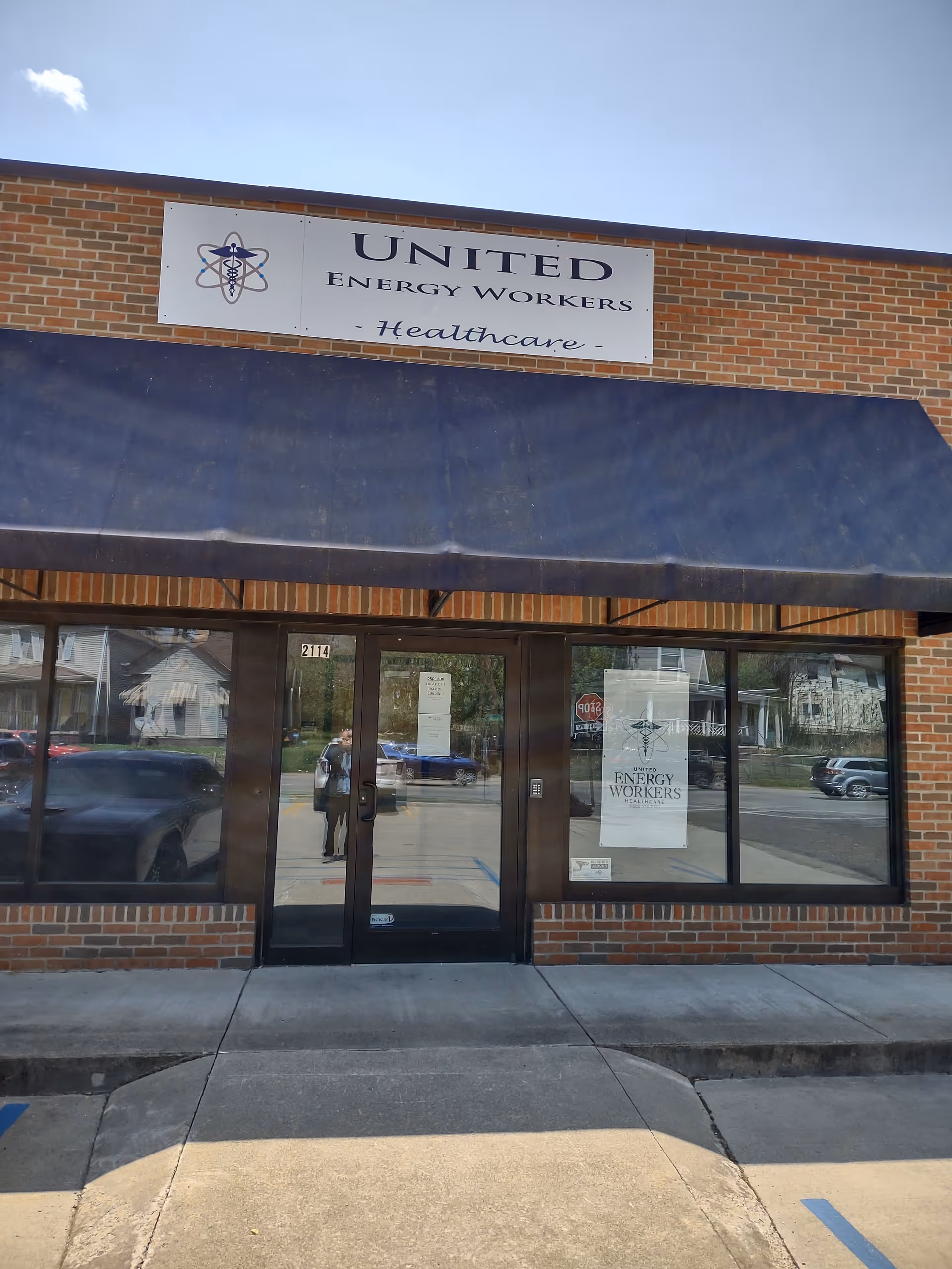 Brick storefront with a large sign reading United Energy Workers Healthcare and a blue awning.