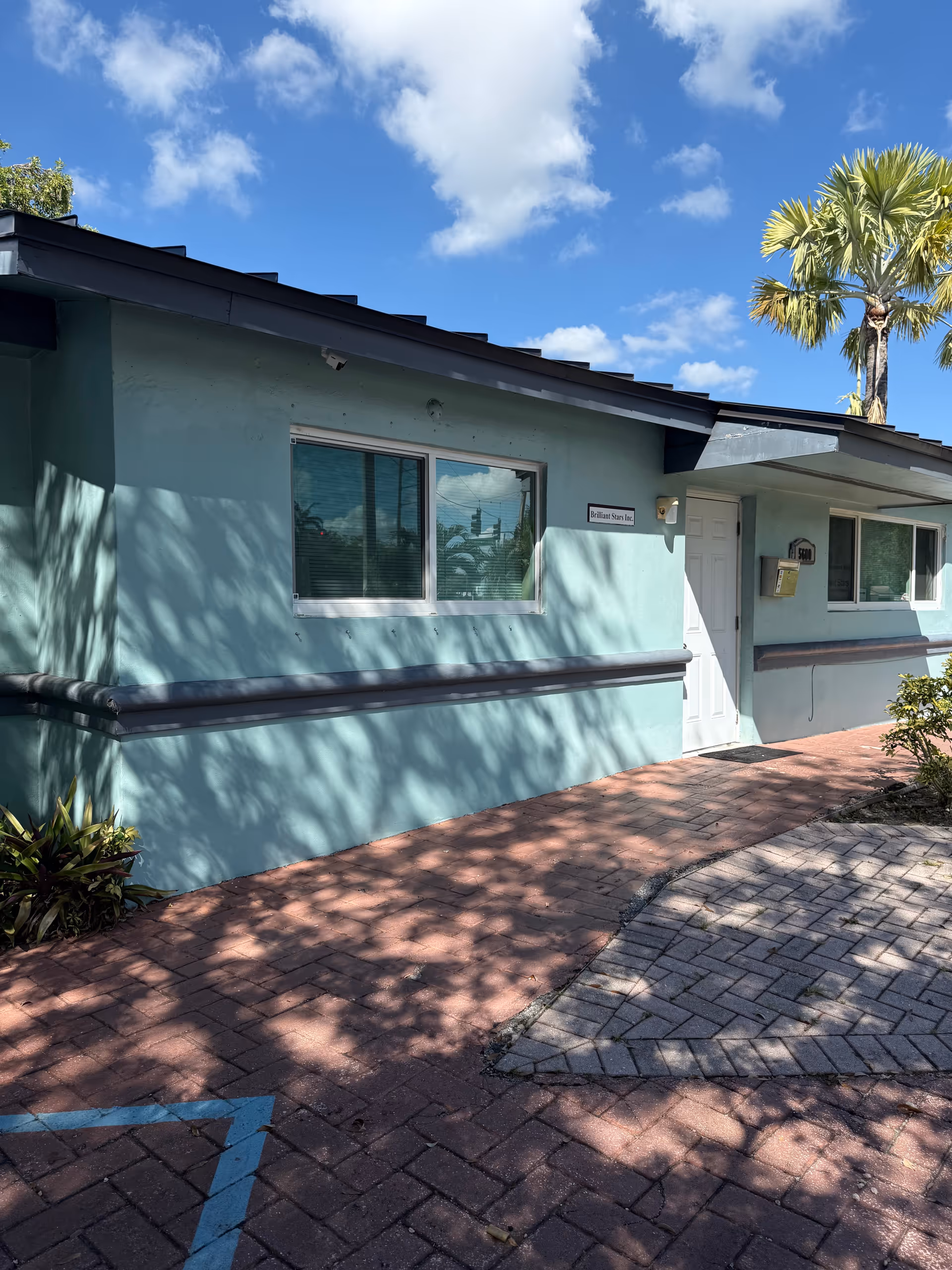 Exterior view of a turquoise senior living facility with windows, door, and a palm tree.