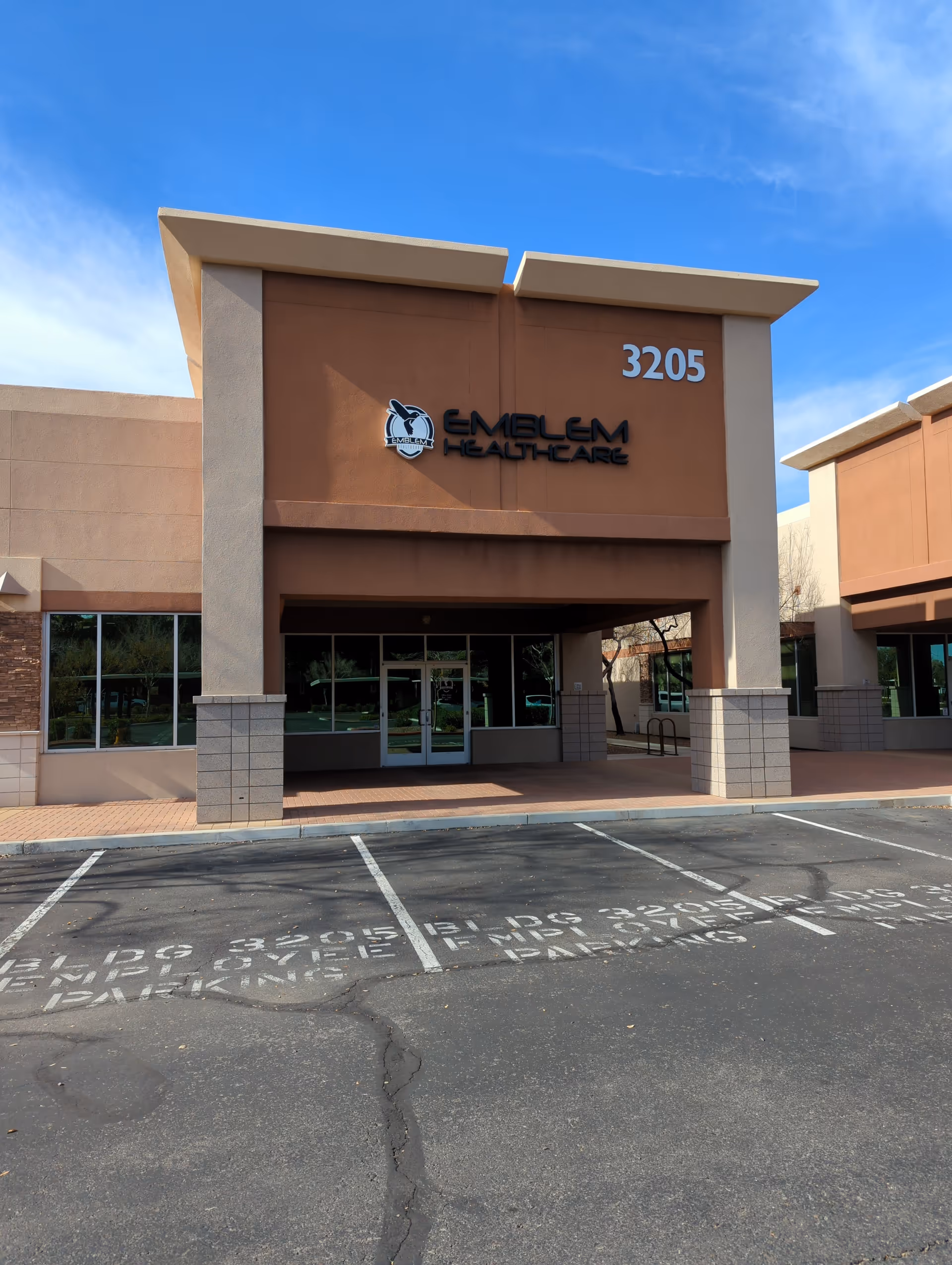 Emblem Healthcare building front entrance with sign and parking lot.