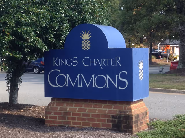 Blue Kings Charter Commons sign on brick pedestal in a parking lot.