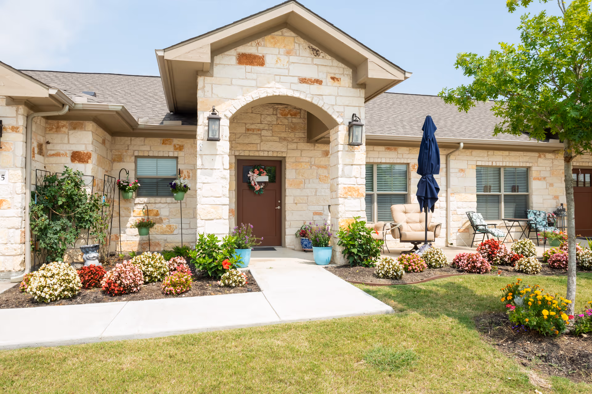 Front entrance of Heritage Lakes Senior Living Community with stone facade, garden flowers, and outdoor seating.