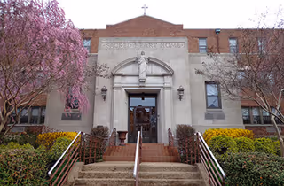 Exterior view of Sacred Heart Free Home entrance with stairs and flowering trees.