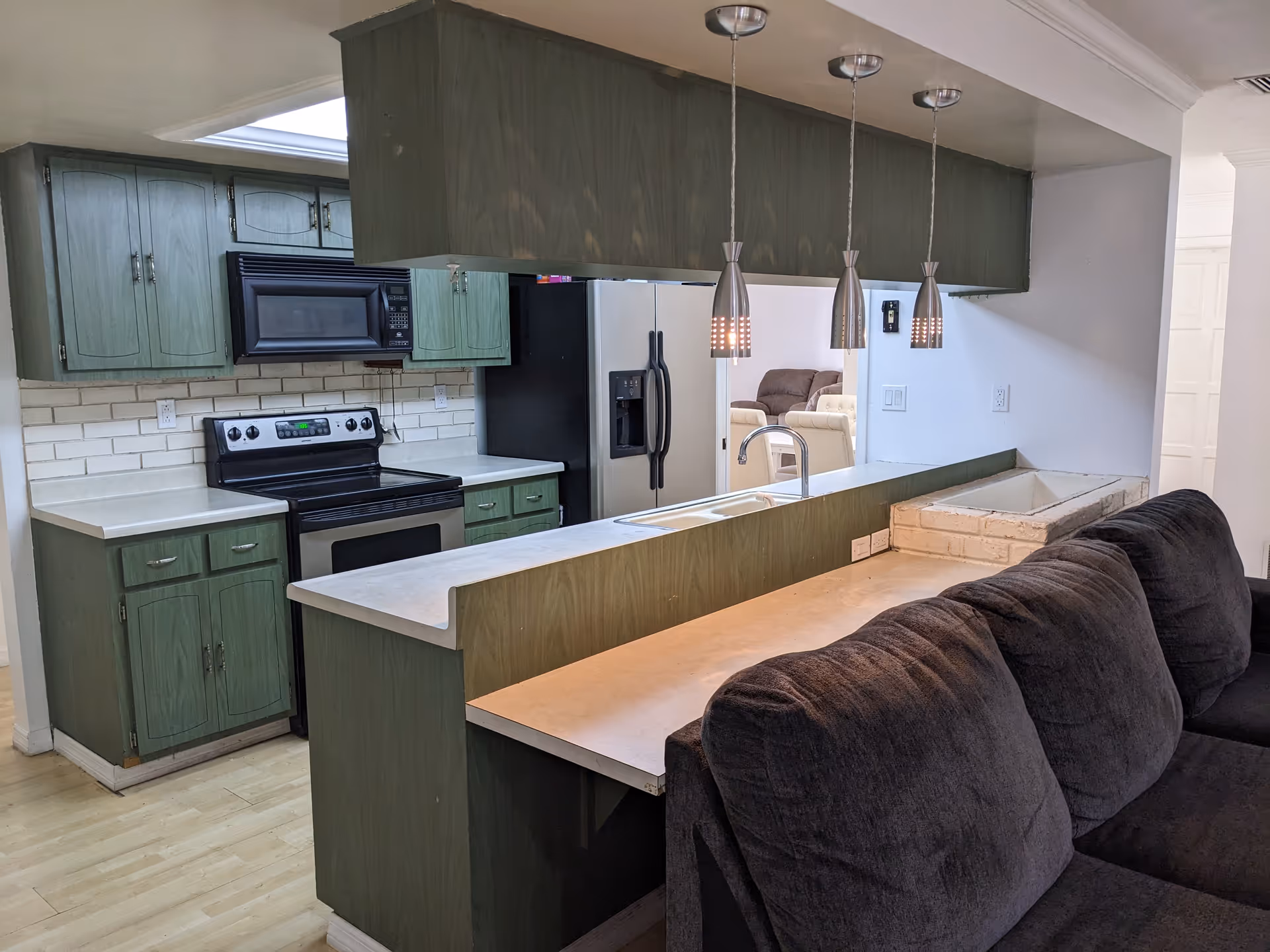 Open-concept kitchen with green cabinets, stainless appliances, and a bar counter beside a sofa.