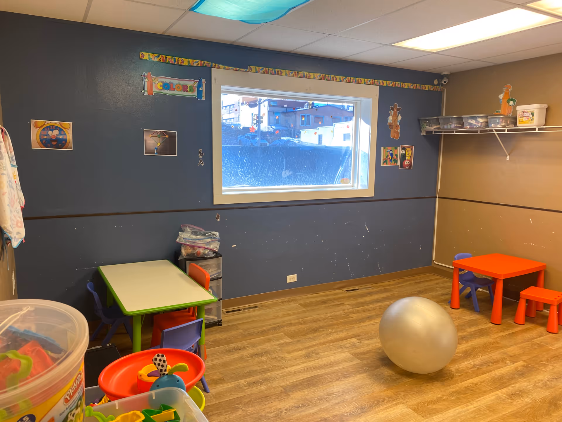 A colorful children's playroom with small tables, chairs, and a large exercise ball.