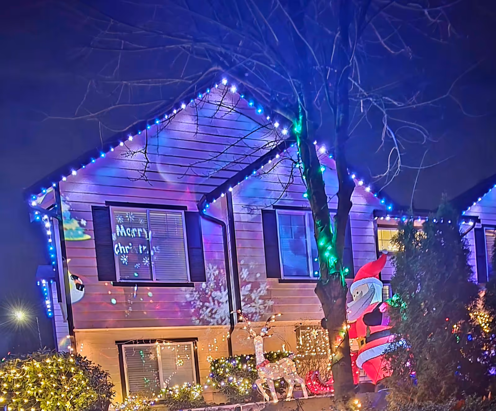 Two-story house decorated with colorful Christmas lights and inflatable holiday figures at night.