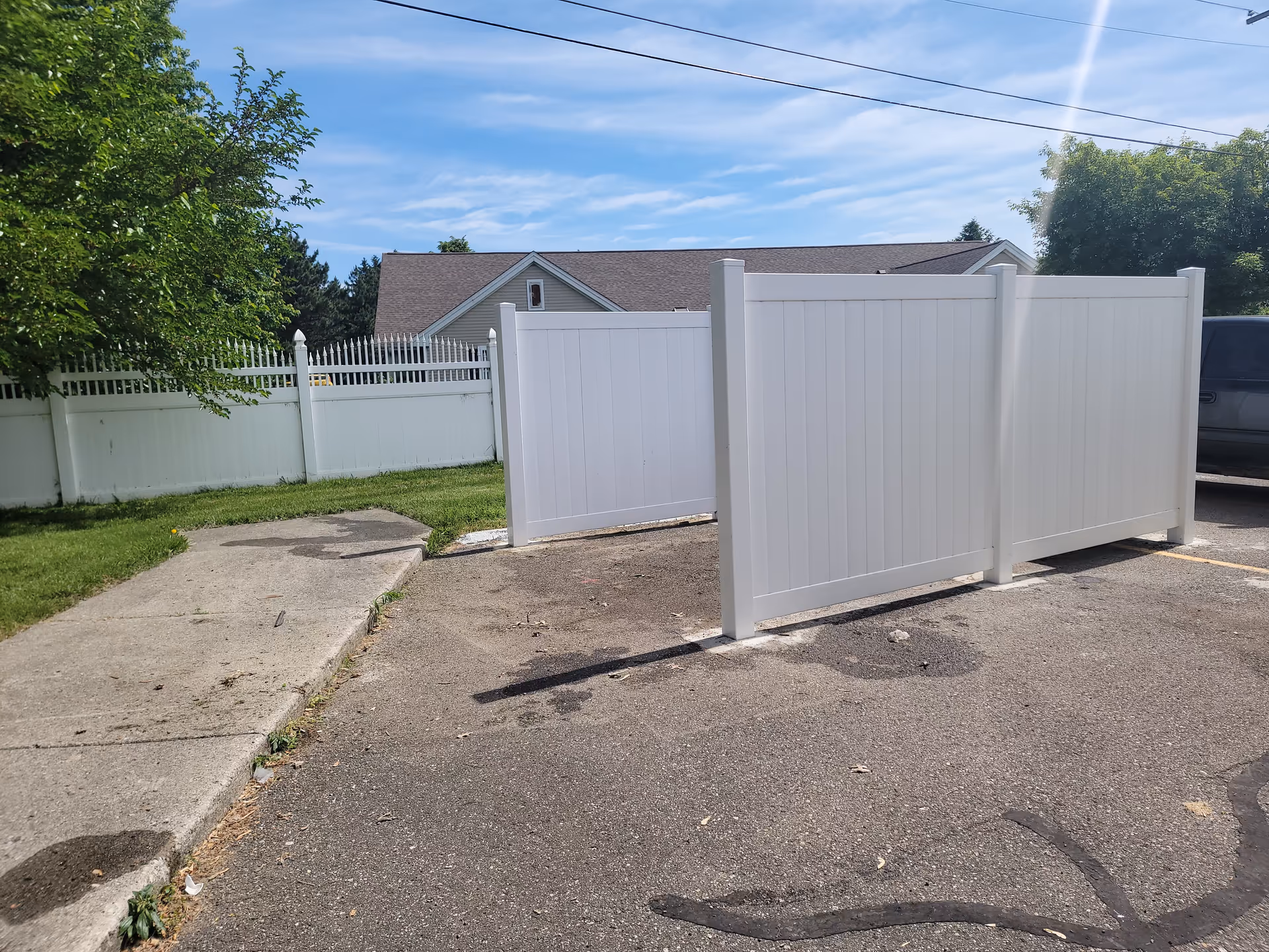 White privacy fence blocks view of a building across a paved lot under blue sky