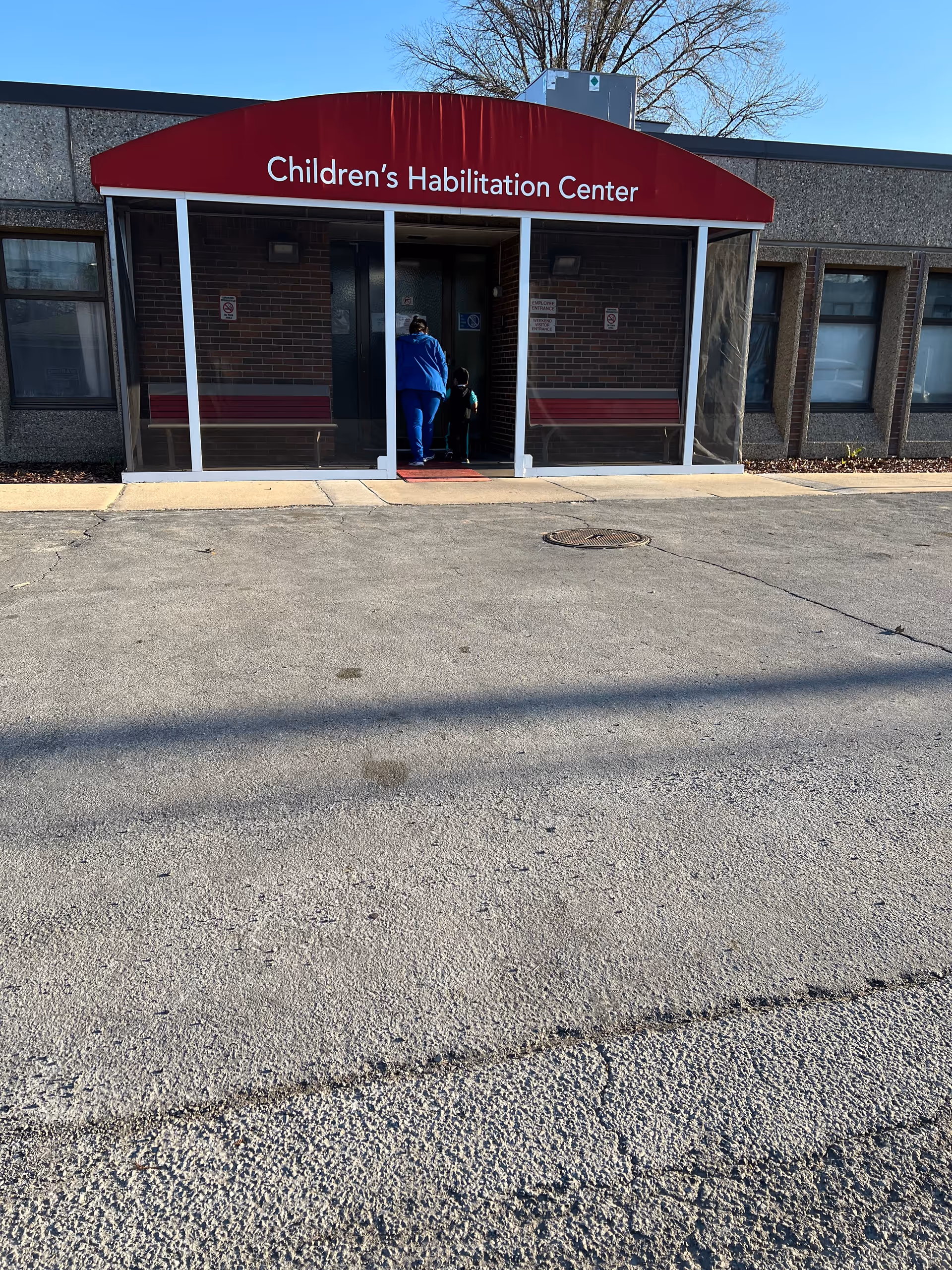 Front entrance of a facility with a red canopy reading Children's Habilitation Center; people entering.