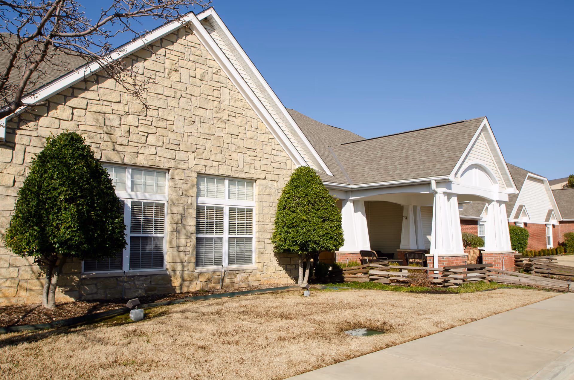 Exterior of Brookdale Claremore senior living with stone facade and front porch seating.