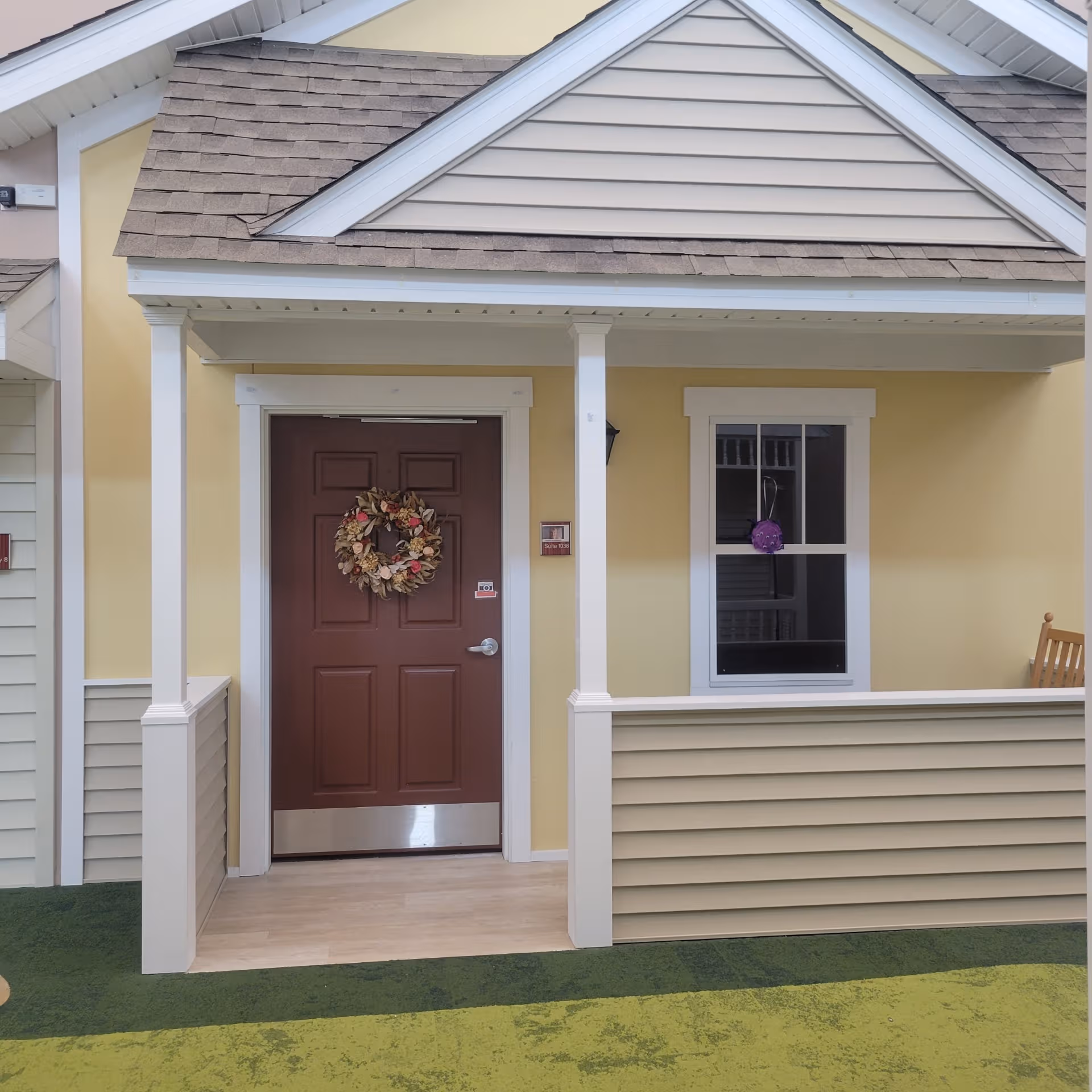 Yellow building entrance with brown door, wreath, and small porch.