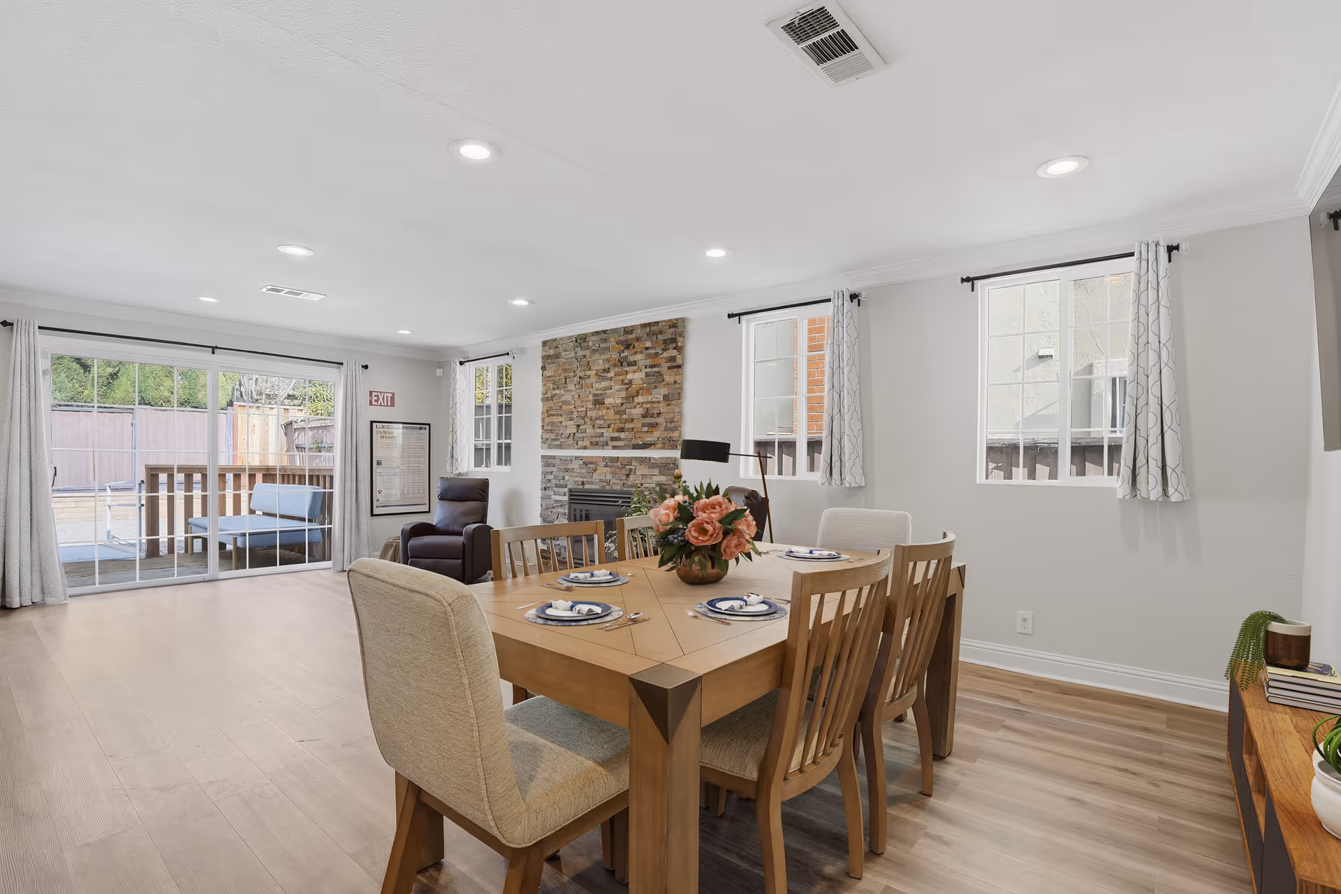 Bright dining room with a wooden table, chairs, fireplace, and large windows.
