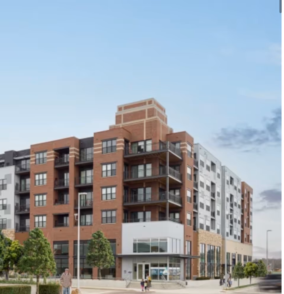 Multi-story brick senior living building with balconies and a glass-front entrance.
